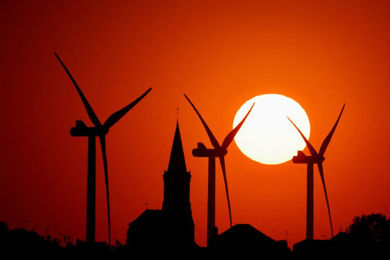 FILE PHOTO: Power-generating windmill turbines and the church of the village are pictured during sunset at a wind park in Bethencourt