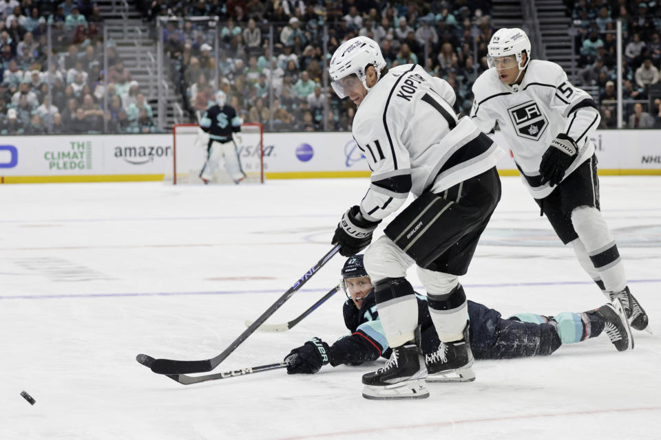 Los Angeles Kings center Anze Kopitar (11) and center Quinton Byfield (55) chase the puck as Seattle Kraken center Jaden Schwartz (17) reaches while lying on the ice during the second period of an NHL hockey game Saturday, April 1, 2023, in Seattle. (AP Photo/John Froschauer)