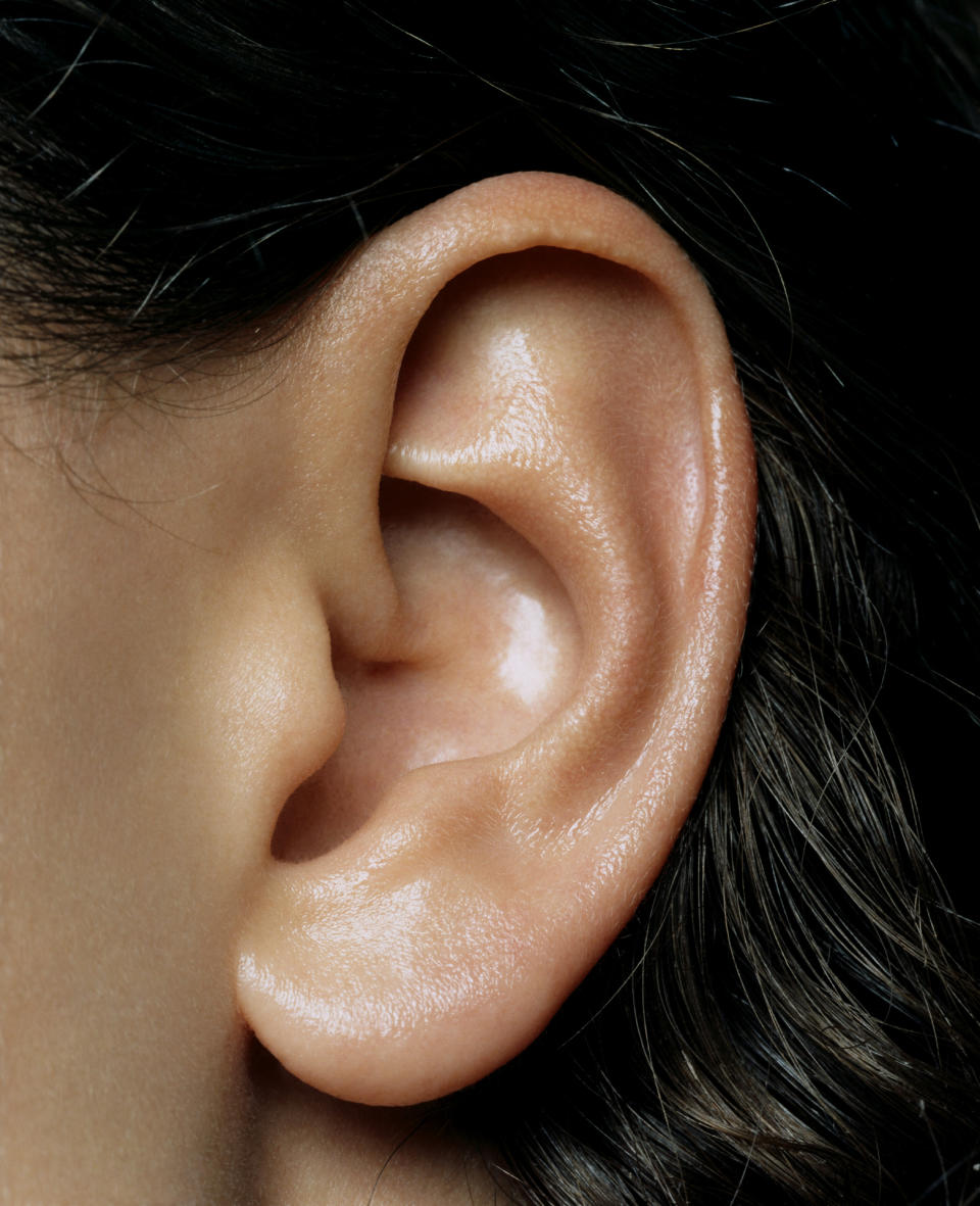 Close-up photo of a human ear with a few strands of hair visible behind it