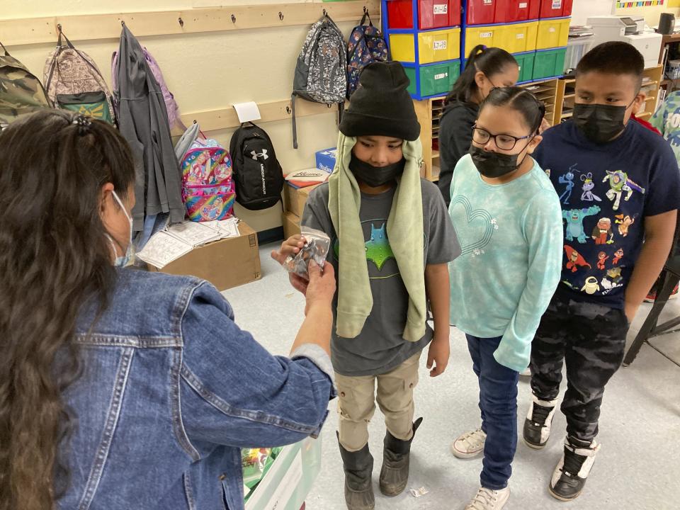 This Feb. 17, 2023 image shows second-grade teacher Adrianne Keene, left, handing out play coins to her students in the Navajo community of To'Hajiilee, New Mexico. To'Hajiilee Community School is just one of dozens funded by the U.S. Bureau of Indian Education that are in desperate need of repair or replacement. The agency estimates it would cost roughly $6.2 billion to address the needs of those schools in poor condition. (AP Photo/Susan Montoya Bryan)