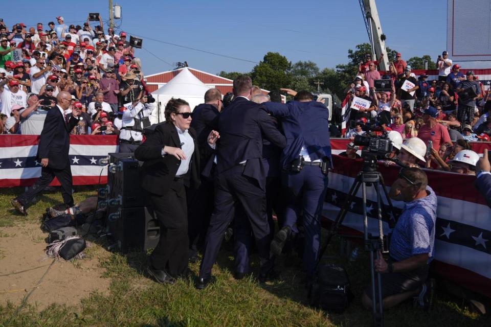 Security agents in suits surround ex-President Trump as spectators look on from stands draped in American flag colors