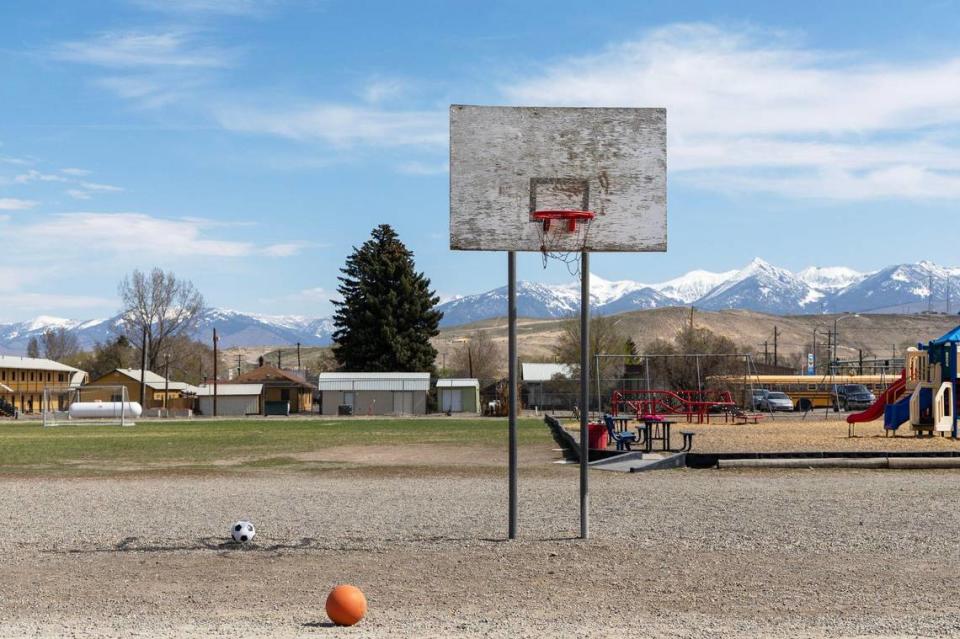 An old basketball hoop stands in front of newer playground equipment on the backside of the elementary school in Salmon.