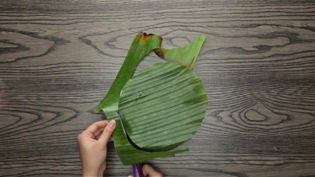 Cutting a circle out of banana leaf with scissors