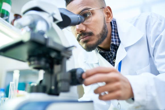 Man in a lab coat peering through a microscope.