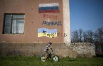 A boy rides a bicycle past a building with Russian and Ukrainian national flags and words reading "Ukraine had sold herself for dollars Russia" in Uspenka village, 4 kilometers (2.8 miles) to the Ukrainian-Russian border, Donbas region, Ukraine, Friday, April 18, 2014. Dashing hopes of progress raised by a diplomatic deal in Geneva, pro-Russian insurgents who have occupied government buildings in more than 10 Ukrainian cities said Friday they will not leave them until the country's interim government resigns. (AP Photo/Evgeniy Maloletka)
