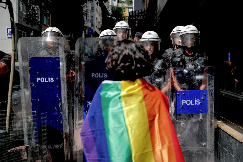 TOPSHOT - A participant faces riot policemen wearing a rainbow flag during a Pride march in Istanbul, on June 26, 2022. - Turkish police forcibly intervened in a Pride march in Istanbul, detaining dozens of demonstrators and an AFP photographer, AFP journalists on the ground said. The governor's office had banned the march around Taksim Square in the heart of Istanbul but protesters gathered nearby under heavy police presence earlier than scheduled. (Photo by KEMAL ASLAN / AFP) (Photo by KEMAL ASLAN/AFP via Getty Images)