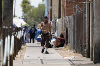 A pedestrian walks along next to a homeless encampment as temperatures continue to soar past 115-degrees Thursday, June 17, 2021, in Phoenix. (AP Photo/Ross D. Franklin)