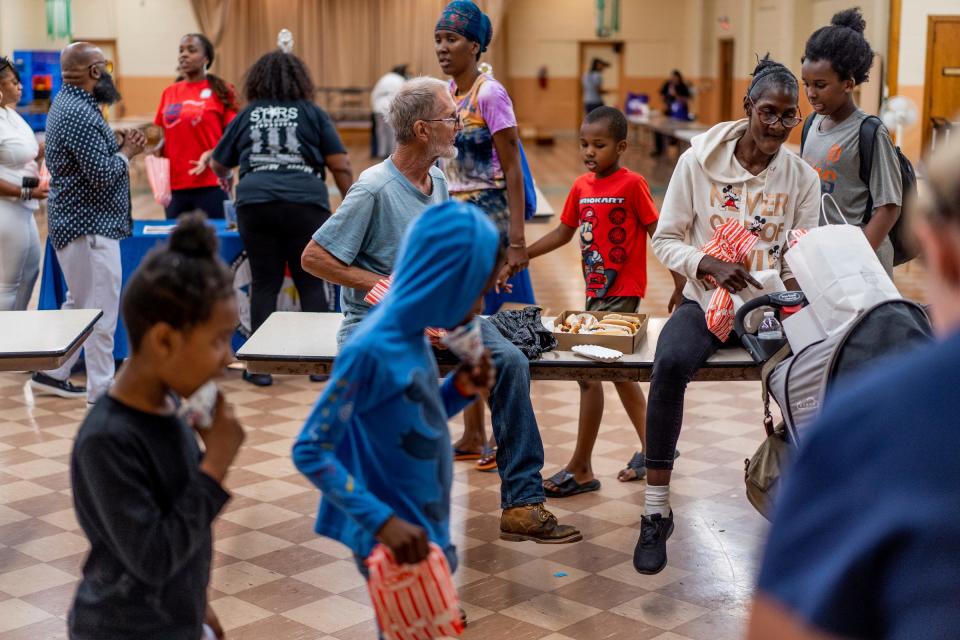 Sir Daniel Albright, center, of Detroit, talks with Tonya Zachery, right, of Detroit, while sitting at a table and eating popcorn during the Community Resource Fair at Christ the King Catholic School in Detroit on Aug. 18, 2023.