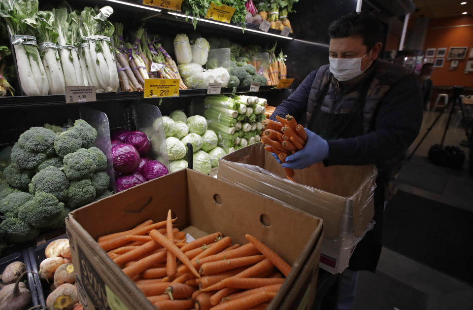 FILE - In this March 27, 2020, file photo, a worker, wearing a protective mask against the coronavirus, stocks produce before the opening of Gus's Community Market in San Francisco. Grocery workers across the globe are working the front lines during lockdowns meant to keep the coronavirus from spreading. (AP Photo/Ben Margot, File)