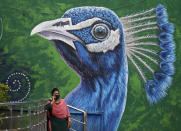 An Indian woman wearing face mask as a precaution against the coronavirus speaks on mobile phone standing in front of a Peacock graffiti on a wall in Hyderabad, India, Thursday, June 17, 2021. (AP Photo/Mahesh Kumar A.)