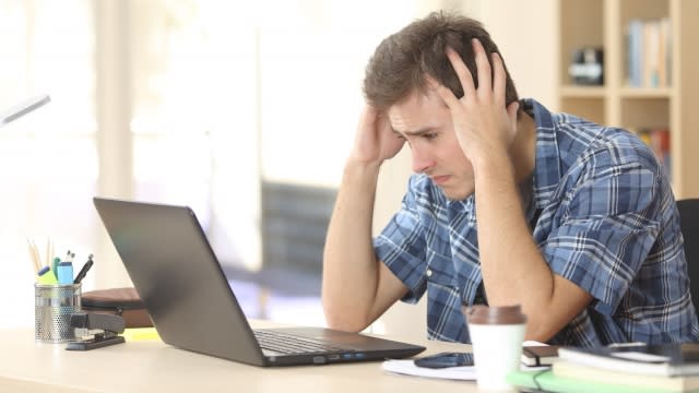 Frustrated student holds head while looking at a laptop