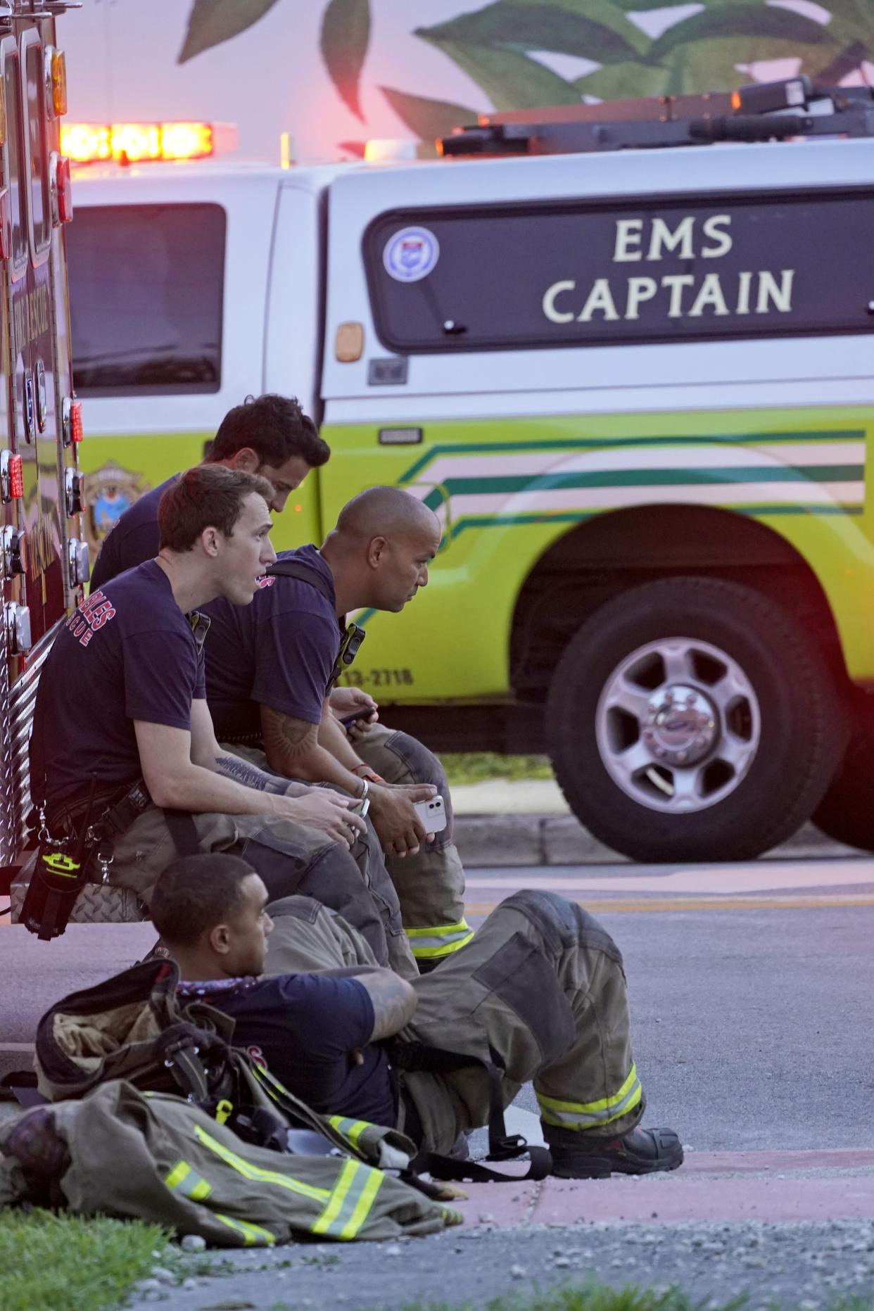 Firefighters wait near the site of a partial building collapse, Thursday, June 24, 2021, in Surfside, Fla.
