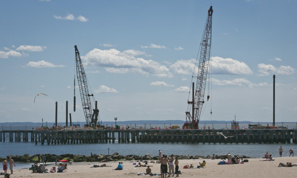 This June 12, 2013 photo shows cranes repairing a pier that was damaged during superstorm Sandy while visitors take to the beach in the Coney Island neighborhood in the Brooklyn borough of New York. (AP Photo/Bebeto Matthews)