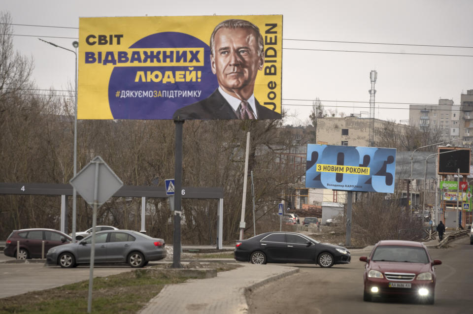 Cars drive past by board depicting US President Joe Biden and reads: "The World of Brave People! #thank you for support", in the town of Bucha, outside Kyiv, Ukraine Jan. 30, 2023. (AP Photo/Efrem Lukatsky)