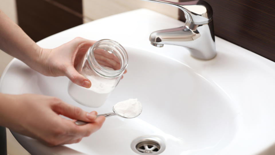 Woman sprinkling a spoonful of borax down sink drain to unclog drain
