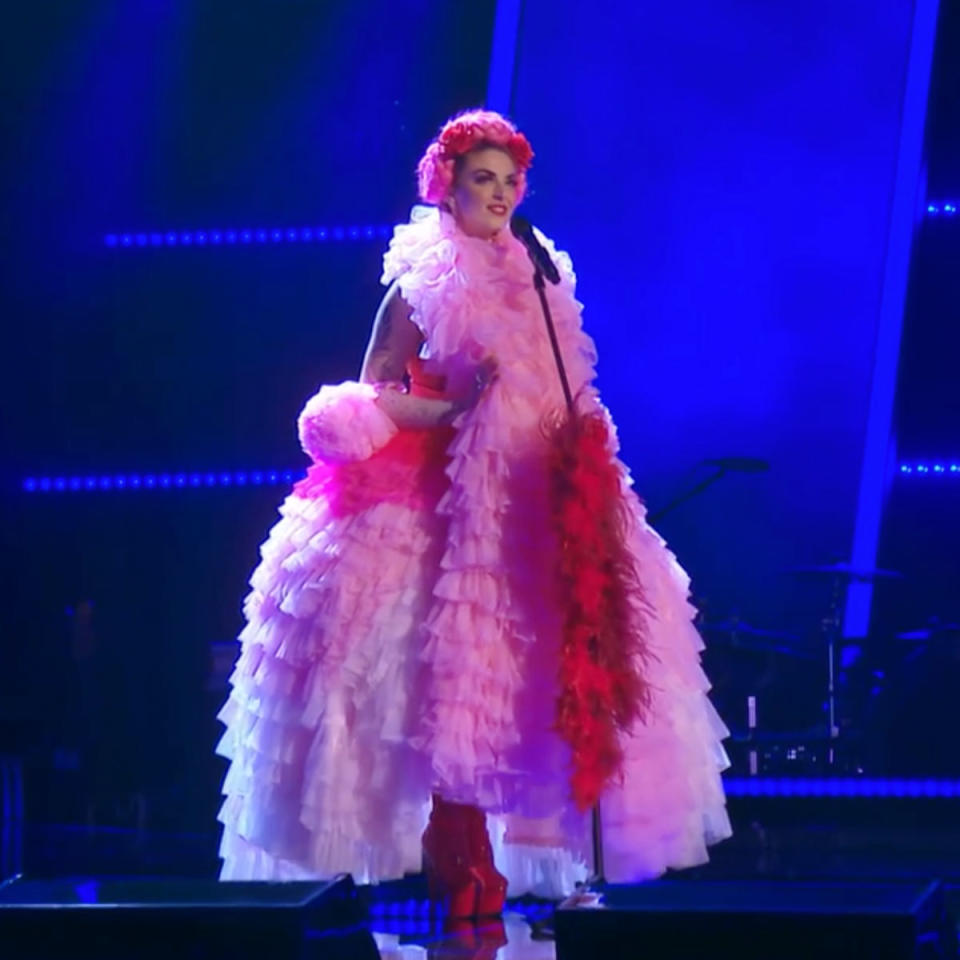 The Voice contestant Lou P Scarlett wears a frilly pink gown with a feather boa. She has a pink headpiece on. 