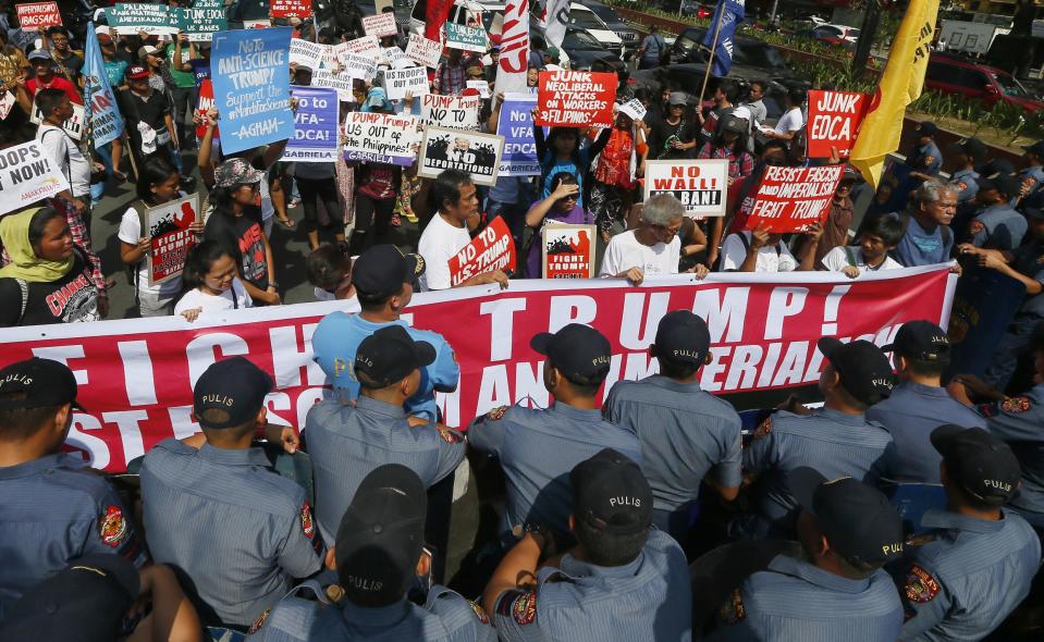 A protester displays placards in front of riot police during a rally at the U.S. Embassy to protest U.S. President Donald Trump's recent anti-immigration policies, Saturday, Feb. 4, 2017, in Manila, Philippines. The protest also marked the Feb. 4, 1899 Filipino-American War. (AP Photo/Bullit Marquez)