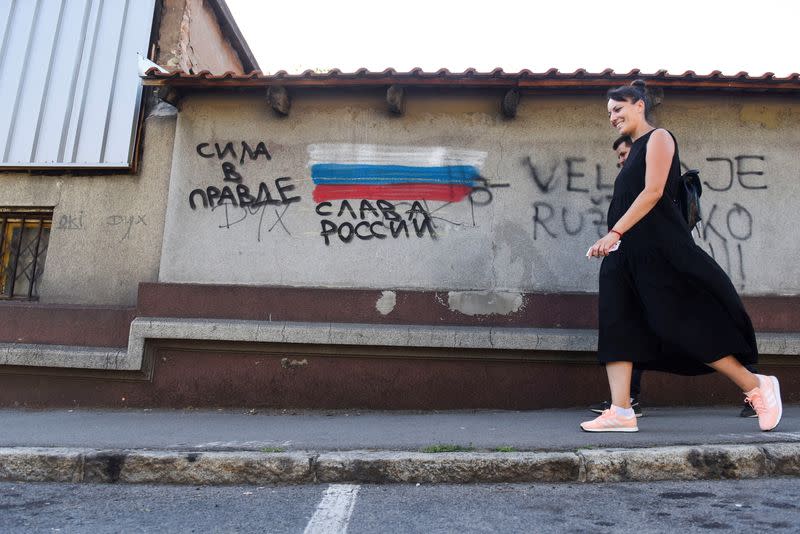 A woman walks next to a graffiti with the words reading "Glory to Russia", in Belgrade