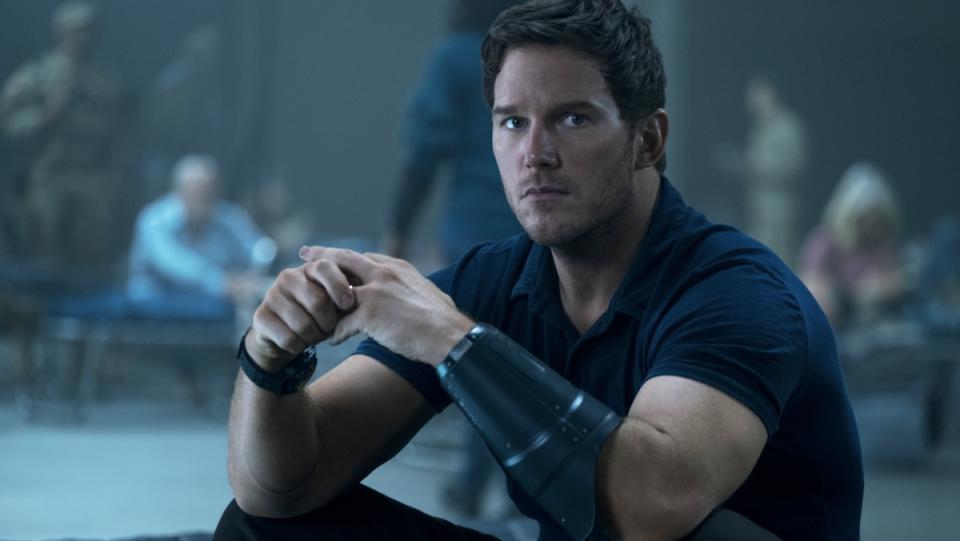 Chris Pratt sits on the floor in a black short sleeved shirt