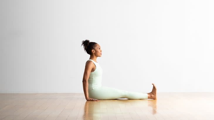 A woman in a mint green tights and top practices Staff Pose, Dandasana