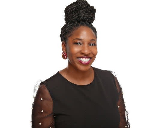 A photo of Raquel Martin, Ph.D., HSP. She is a Black woman, smiling warmly at the camera. She has her twists in a top knot. She is wearing a black shirt with sheer sleeves decorated in pearls. She has round earrings with a pattern.