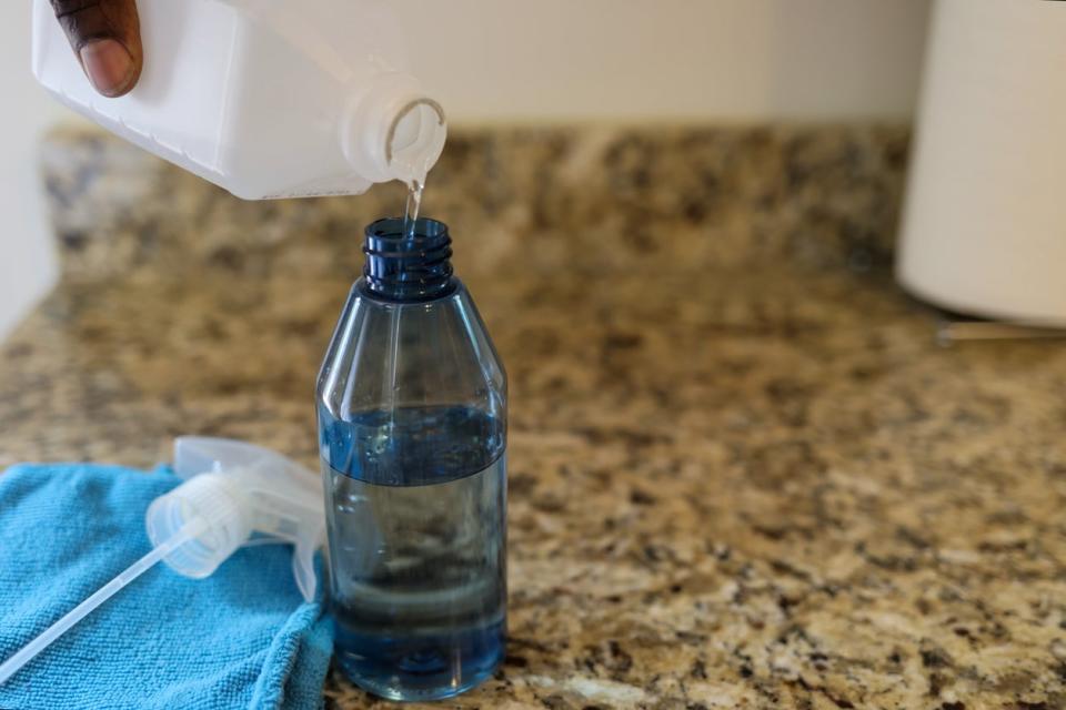 close shot of woman's hand holding bottle of rubbing alcohol and pouring it into a spray bottle on a marble kitchen counter top