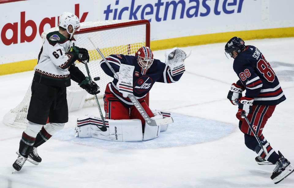 Arizona Coyotes' Lawson Crouse (67) attempts to tip the puck past Winnipeg Jets goaltender Laurent Brossoit (39) as Nate Schmidt (88) defends during the second period of an NHL hockey game, Saturday, Nov. 18, 2023 in Winnipeg, Manitoba. (John Woods/The Canadian Press via AP)