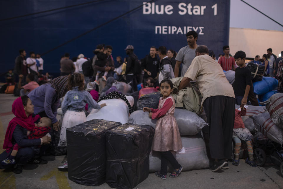 On this Tuesday, Oct. 1, 2019 photo, an Afghan child stands next her family's belongings after disembarking from a ferry with other refugees and migrants at the port of Piraeus, near Athens. Greece's conservative government announced Wednesday Nov. 20, 2019, plans to overhaul the country's migration management system, and replacing existing camps on the islands with detention facilities and moving and 20,000 asylum seekers to the mainland over the next few weeks. (AP Photo/Petros Giannakouris)