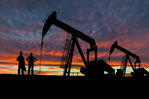 A silhouette of two people near some oil pumps at sunset.