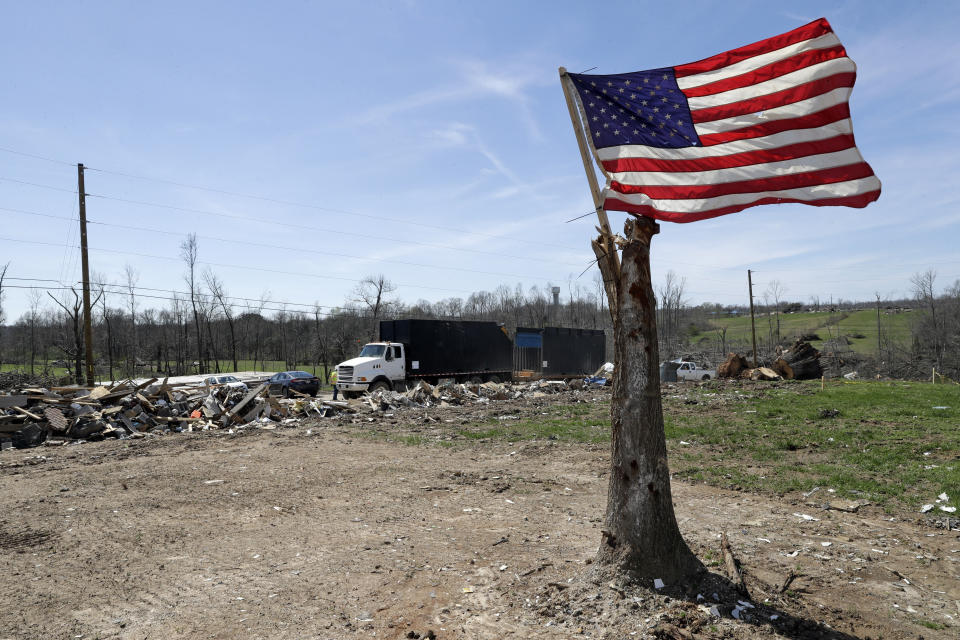 In this March 26, 2020, photo, a flag flies from a tree trunk on a lot stripped of buildings in Cookeville, Tenn. People still reeling from the deadly twisters that hit the state on March 3 now have to confront life in the age of coronavirus. (AP Photo/Mark Humphrey)