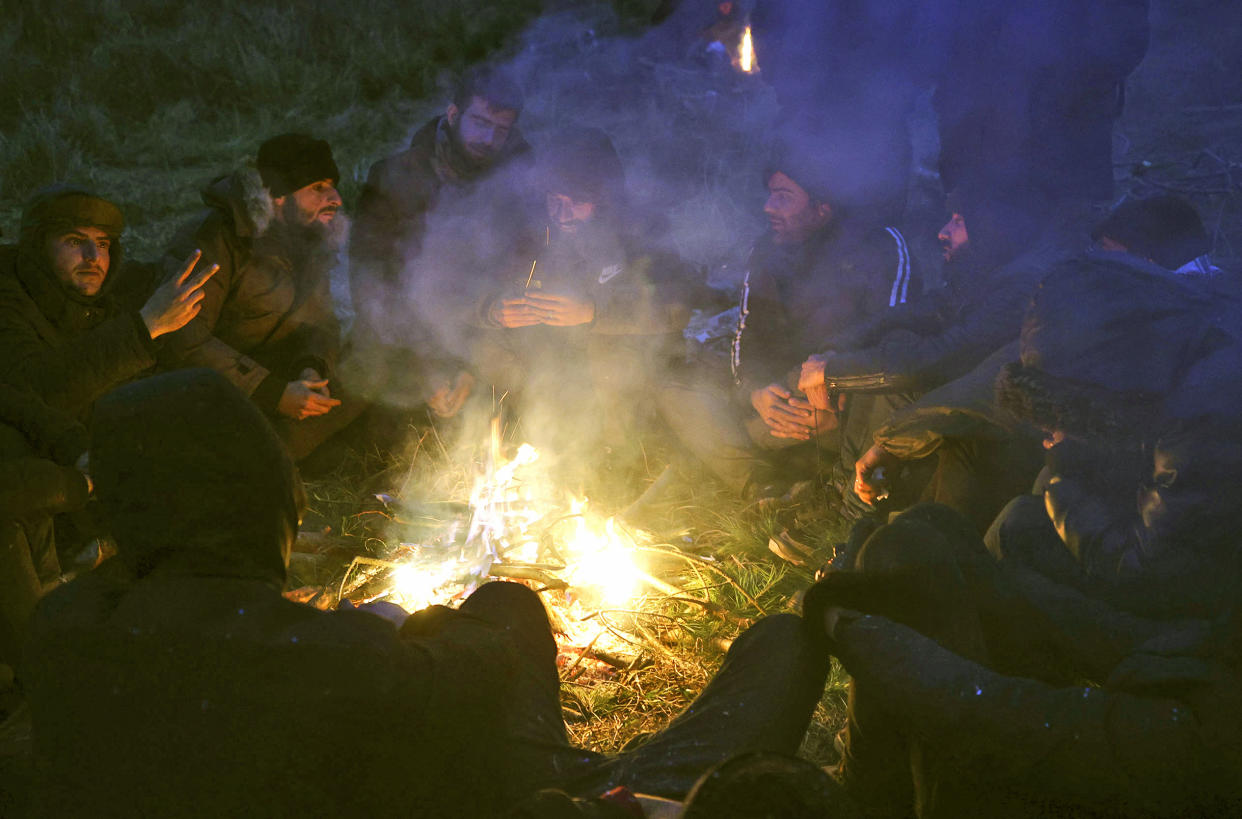 Migrants warm themselves near fire gathering at the checkpoint "Kuznitsa" at the Belarus-Poland border near Grodno, Belarus, on Monday, Nov. 15, 2021. The EU is calling for humanitarian aid as up to 4,000 migrants are stuck in makeshift camps in freezing weather in Belarus while Poland has reinforced its border with 15,000 soldiers, in addition to border guards and police. (Leonid Shcheglov/BelTA via AP)