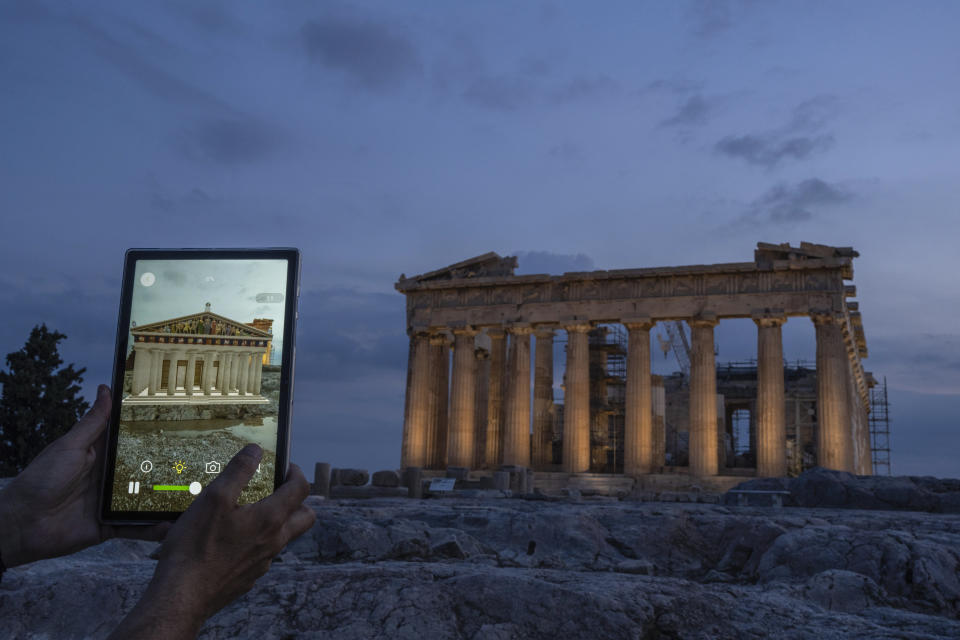 A man holds up a tablet showing a digitally overlayed virtual reconstruction of the ancient Parthenon temple, at the Acropolis Hill in Athens, Greece on Tuesday, June 13, 2023. Greece has become a late but enthusiastic convert to new technology as a way of displaying its famous archaeological monuments and deepening visitors' knowledge of ancient history. The latest virtual tour on offer is provided by a mobile app that uses Augmented Reality to produce digital overlays that show visitors at the Acropolis how the site and its sculptures looked 2,500 ago. (AP Photo/Petros Giannakouris)