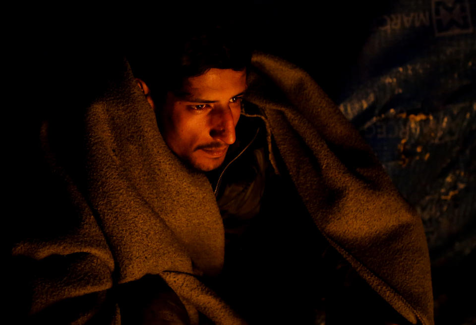 In this Sunday, Nov. 18, 2019 photo a migrant warms himself next to a fire at a camp in Velika Kladusa, Bosnia, close to the border to Croatia. The approach of the tough Balkan winter spells tough times for the migrants that remain stuck in the region while trying to reach Western Europe, with hundreds of them staying in make-shift camps with no heating or facilities.(AP Photo/Amel Emric)