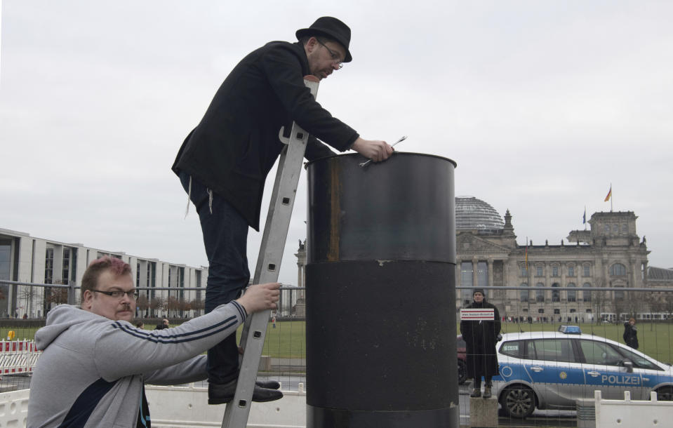 The author Eliyah Havemann reattaches a previously dismantled steel plate to the controversial steel column of the artists' collective "Centre for Political Beauty" (ZPS) opposite the Reichstag building in Berlin Germany, Sunday, Jan.5, 2019. Several activists have tried to dismantle the controversial steel column of the artists' collective "Centre for Political Beauty" (ZPS) in Berlin. "One should not make art and politics with ashes of victims of the Holocaust," Havemann told the dpa on Sunday, explaining the reasons. The police stopped the action and ZPS filed a complaint. (Paul Zinken/dpa via AP)