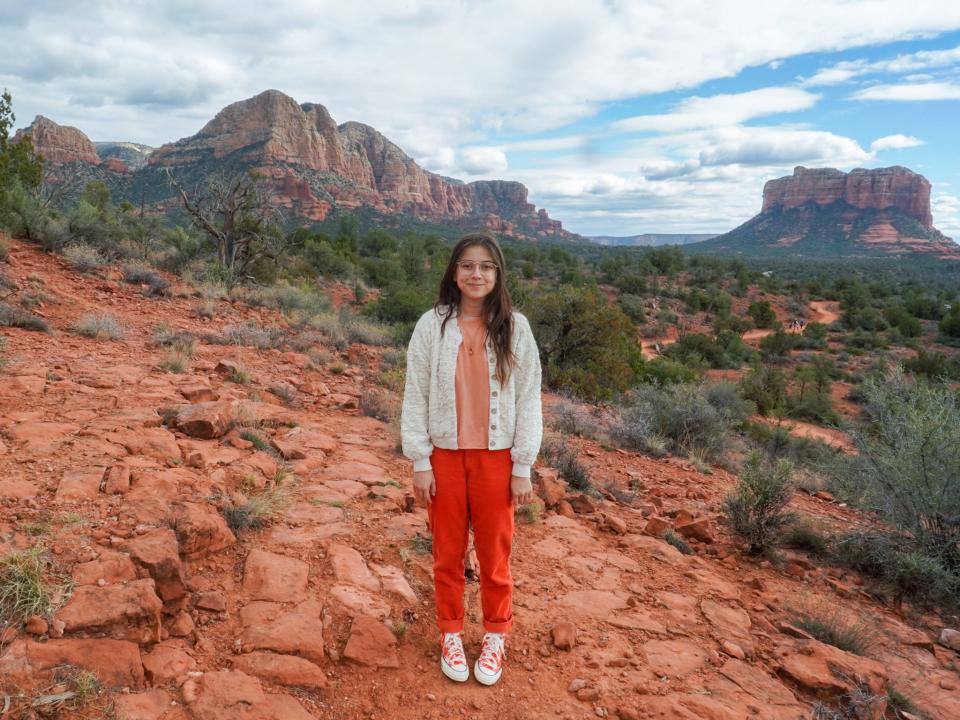 The author stands on red rocks in Sedona with larger rocks and cloudy skies in the background