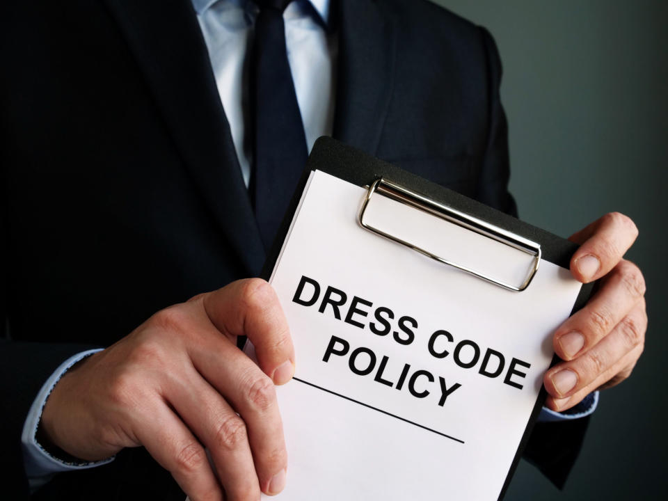 Man holding a clipboard reading "dress code policy"