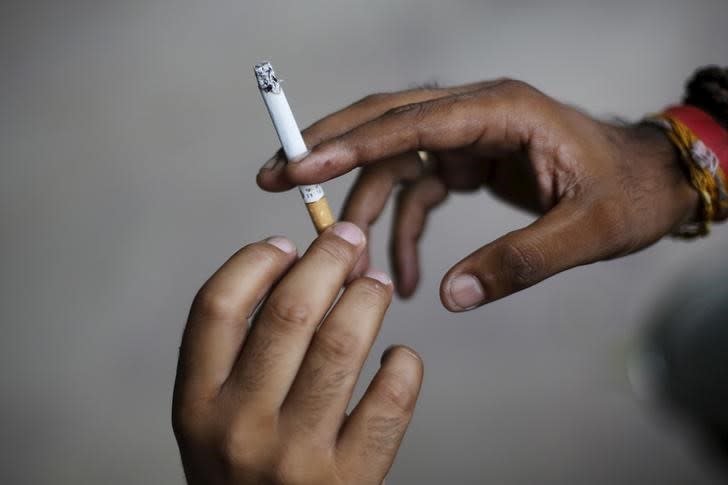 A man passes a cigarette to another while smoking as they sit on a pavement along a road in New Delhi, India, August 18, 2015.  REUTERS/Adnan Abidi