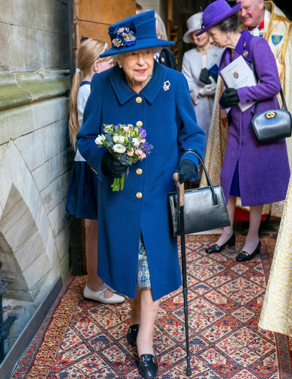 Queen Elizabeth walks with the help of a cane outside of Westminster Abbey.