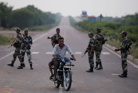 Paramilitary soldiers stand guard as a man rides a motorcycle on a closed road leading to Sunariya Jail in Rohtak in Haryana, India, August 27, 2017. REUTERS/Adnan Abidi