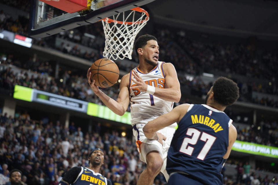 Phoenix Suns guard Devin Booker, back, passes the ball as Denver Nuggets guard Jamal Murray defends in the second half of Game 2 of an NBA second-round playoff series Monday, May 1, 2023, in Denver. (AP Photo/David Zalubowski)
