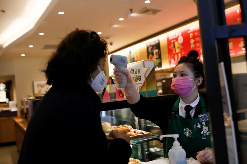 FILE PHOTO: Worker uses a thermometer to check the temperature of a customer as she enters a Starbucks shop as the country is hit by an outbreak of the new coronavirus, in Beijing