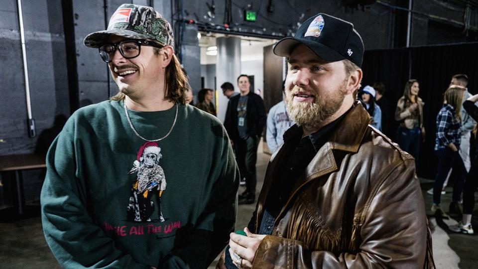 Hardy sports a green sweater and camouflaged hat next to Ernest in a brown leather coat with fringe.