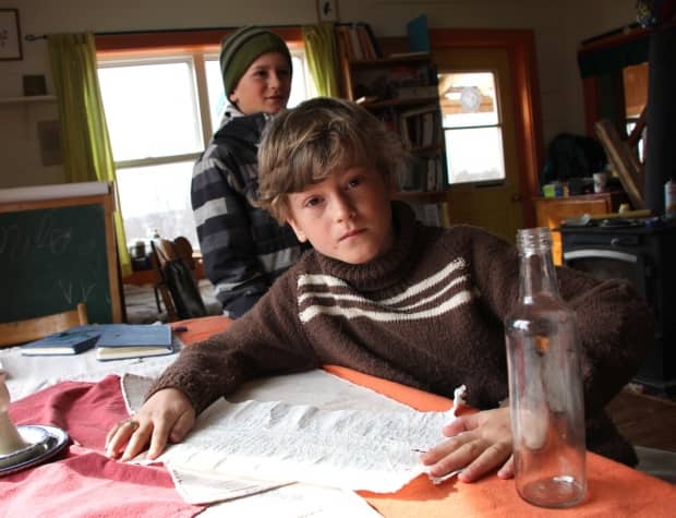 Nyima Mitchell, eight, is shown with the message in a bottle he found in his backyard on the Petit &#xc9;tang, near Ch&#xe9;ticamp, last fall. In the background is his older brother, Mila. (Erin Pottie/CBC - image credit)