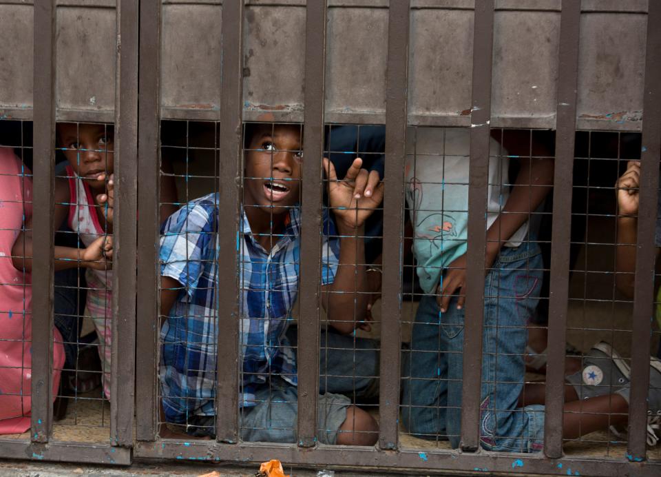 Un niño migrante llama a un vendedor ambulante que vende agua mientras espera junto a otros niños, dentro de un área de la oficina de la  Comisión Mexicana de Ayuda a los Refugiados, a que sus padres llenen formas en Tapachula, México, el viernes 26 de abril del 2019. Miles de migrantes permanecen en la frontera al sur de México esperando por documentos que les permitan permanecer legalmente en el país. (AP Photo/Moises Castillo)