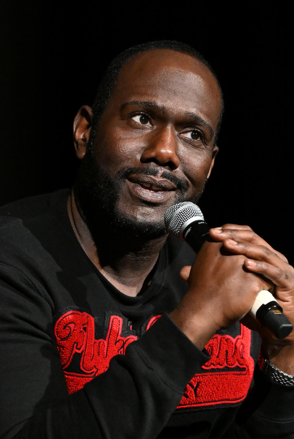 Man in a black sweater with text speaking into a microphone