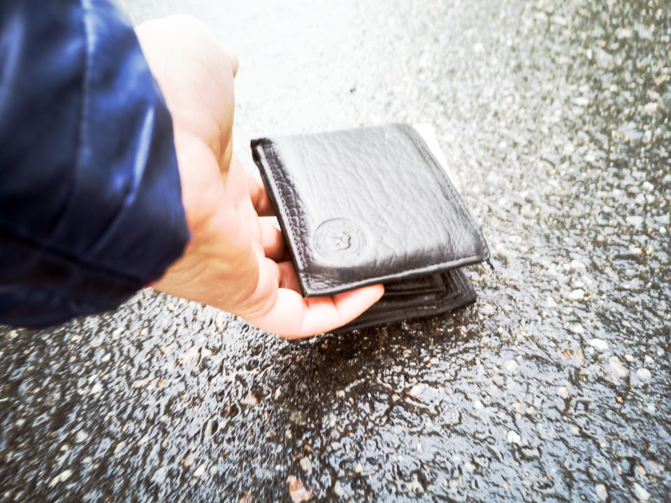 hand picking up a wallet in the road