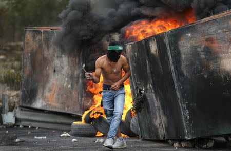 A Palestinian protester takes cover during clashes with Israeli troops near the Jewish settlement of Bet El, near the West Bank city of Ramallah October 23, 2015. REUTERS/Mohamad Torokman