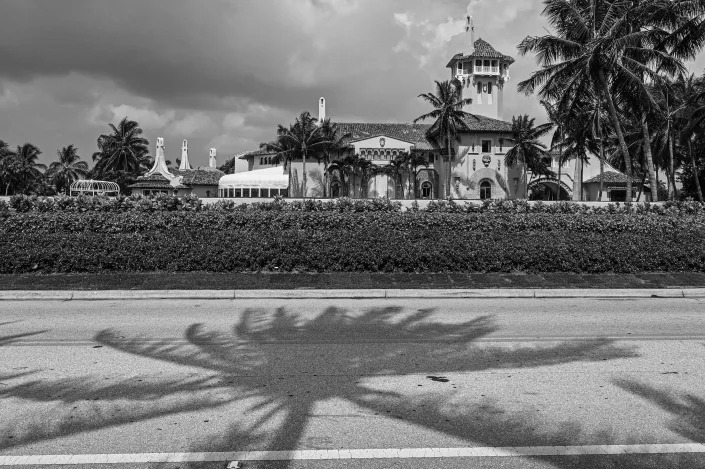 A view of the buildings of Mar-a-Lago from the road, amid palm trees.