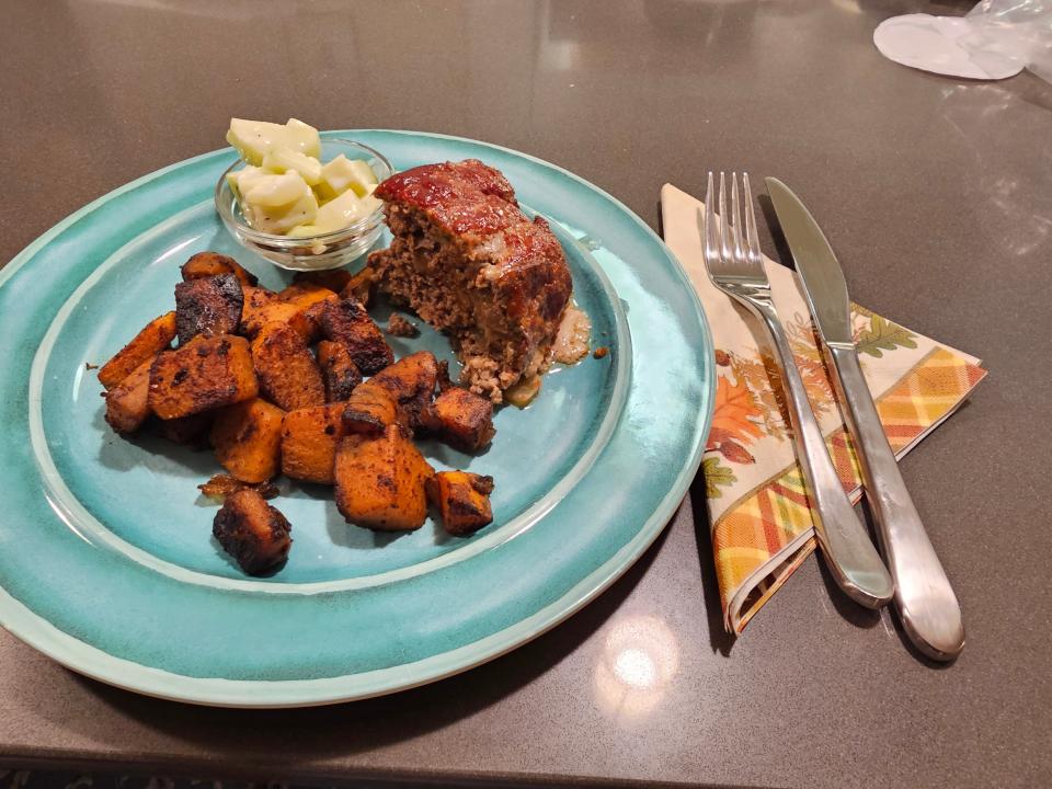 Slice of meatloaf with sweet potatoes on a blue plate next to folded napkin with knife and fork on top of it