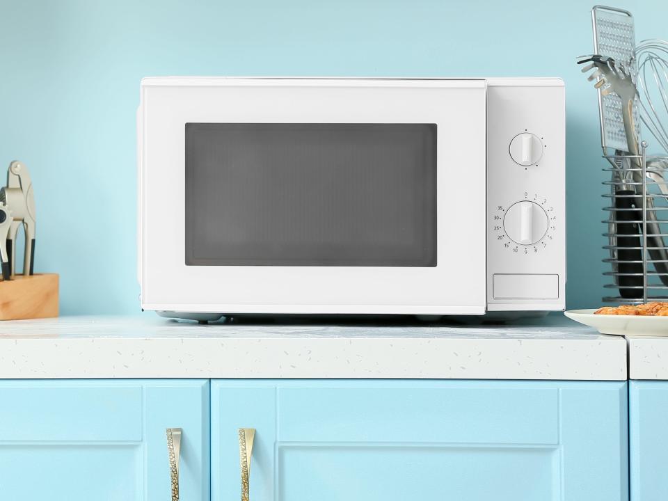 A white microwave on a blue cabinet in front of a blue wall